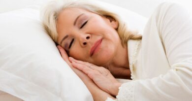 Mulher madura dormindo tranquilamente em uma cama branca, simbolizando os benefícios do sono para a saúde.