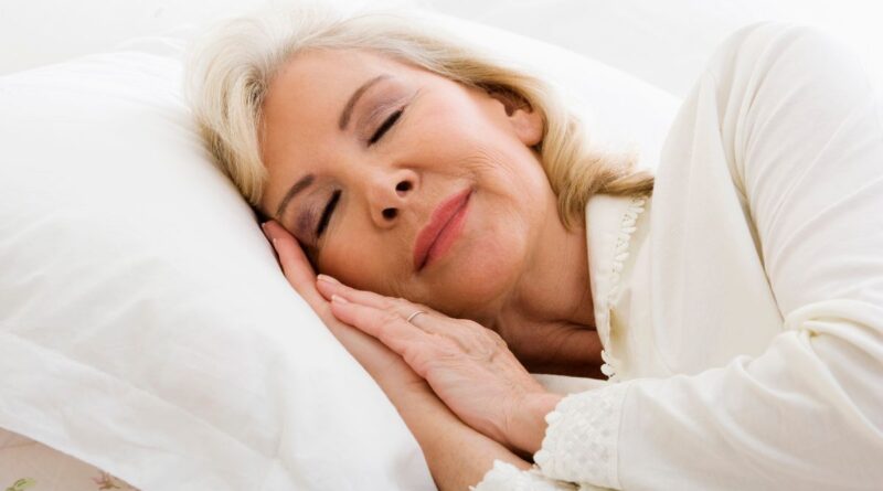 Mulher madura dormindo tranquilamente em uma cama branca, simbolizando os benefícios do sono para a saúde.